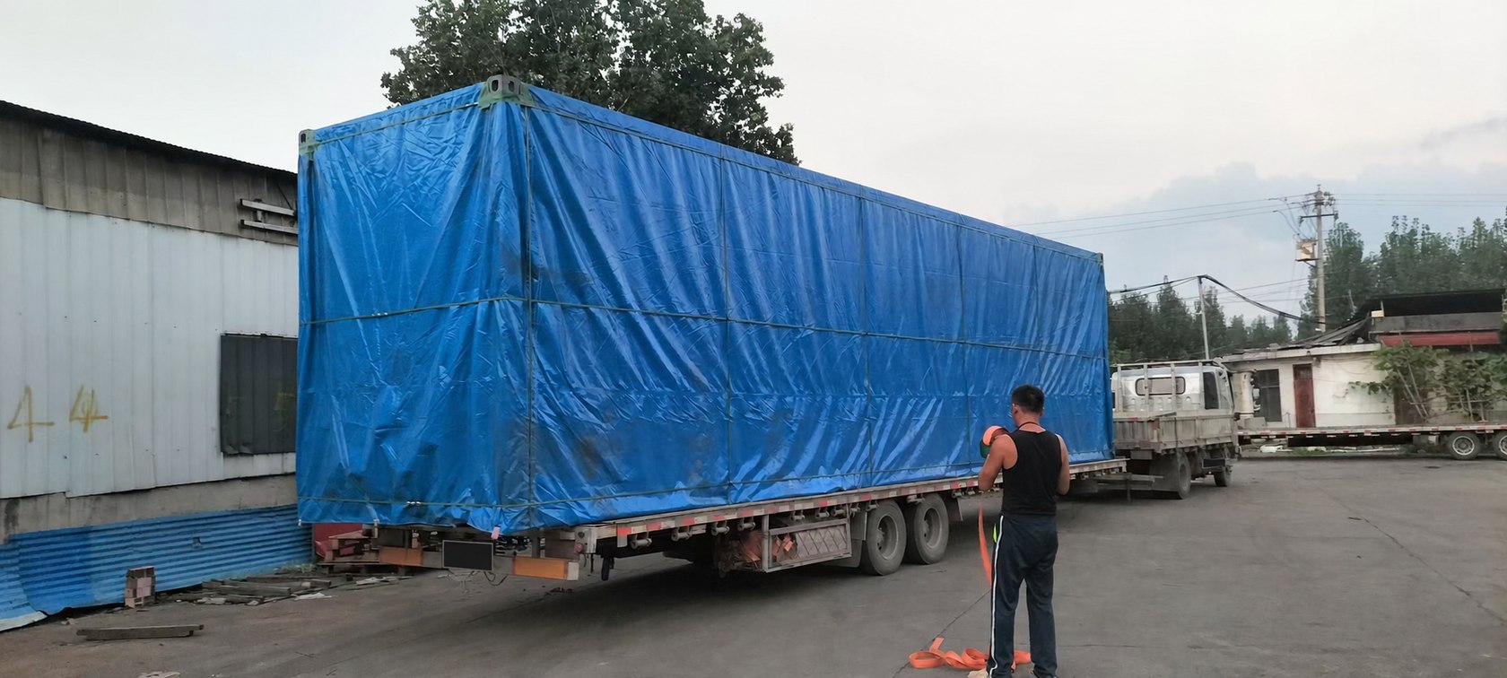 集装箱看台防雨布包装装车。包装装车:整套产品覆盖防雨布;车辆号牌已作AI遮挡处理。