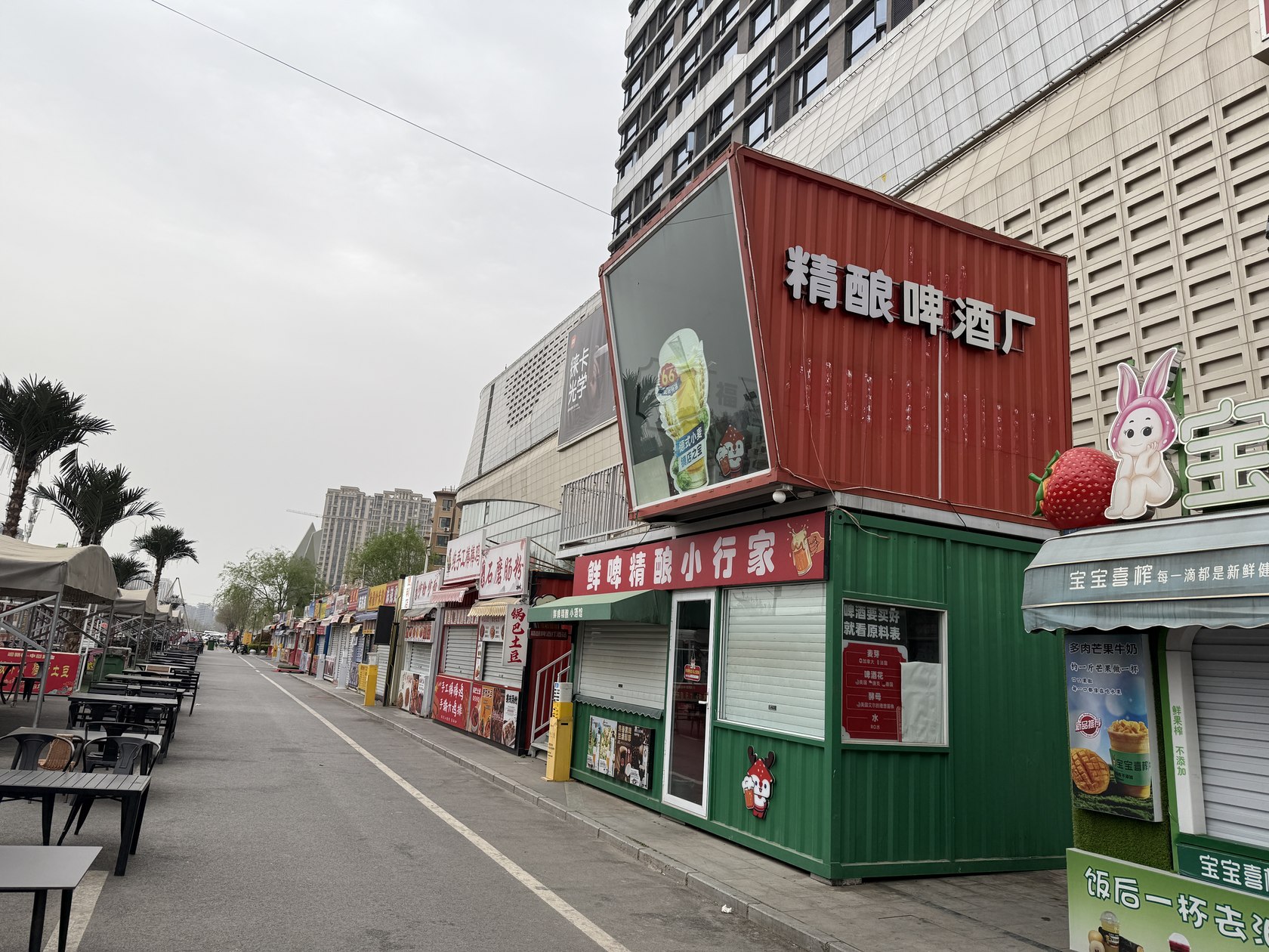 郑州新郑龙湖锦艺城附近集装箱商铺使用阶段街景,可见两层啤酒屋、相邻商铺和街道桌椅。