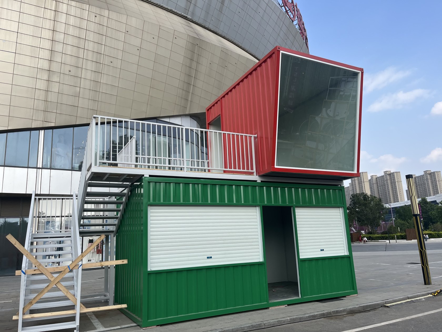 河南郑州新郑两层集装箱啤酒屋安装后实拍,上层为斜角玻璃面,下层可见卷帘开口与玻璃门。